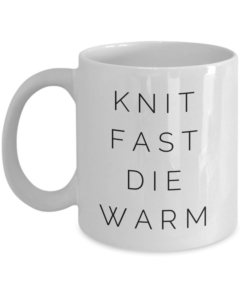 May include: White ceramic mug with black text that reads "Knit Fast Die Warm".