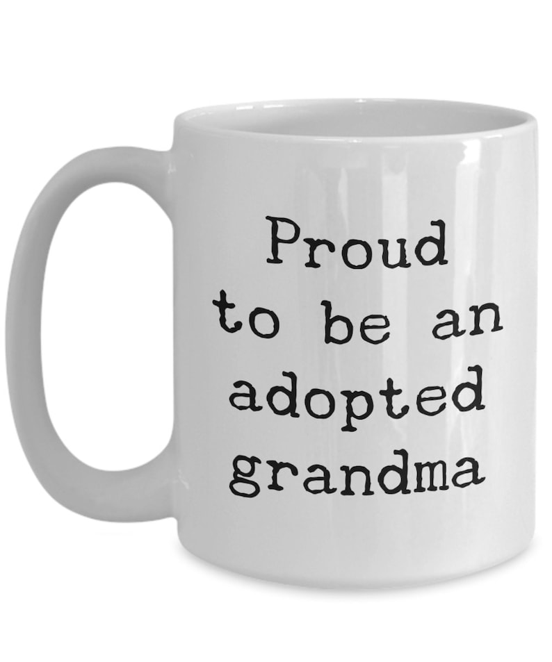 May include: White ceramic coffee mug with black text that reads "Proud to be an adopted grandma".
