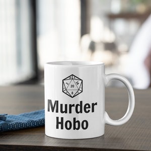 K&ouml;nnte beinhalten: Eine wei&szlig;e Keramiktasse mit einer schwarz-wei&szlig;en Illustration eines zwanzigseitigen W&uuml;rfels und dem Text "Murder Hobo".