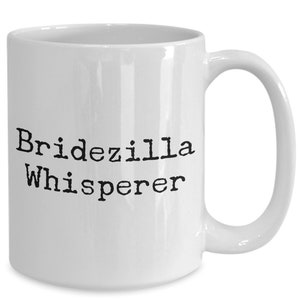 May include: White ceramic coffee mug with black text that reads "Bridezilla Whisperer".