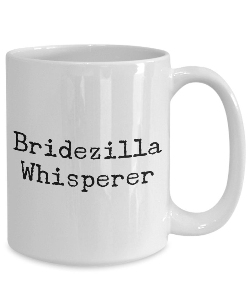 May include: White ceramic coffee mug with black text that reads "Bridezilla Whisperer".