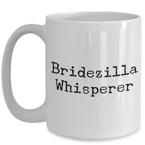 May include: White ceramic coffee mug with black text that reads "Bridezilla Whisperer".