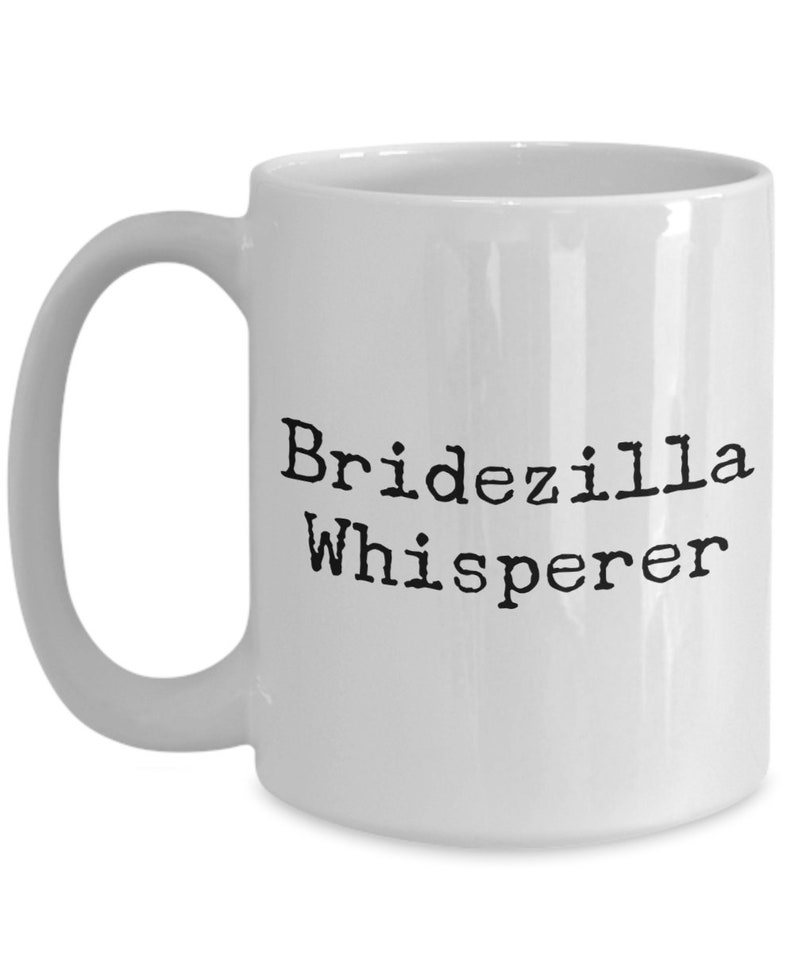 May include: White ceramic coffee mug with black text that reads "Bridezilla Whisperer".