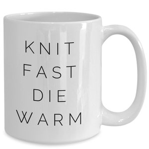 May include: White ceramic coffee mug with black text that reads "Knit Fast Die Warm".