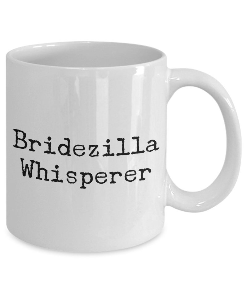 May include: White ceramic coffee mug with black text that reads "Bridezilla Whisperer".