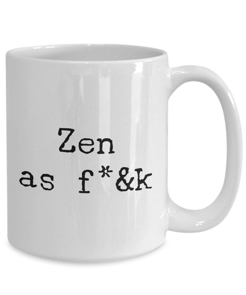 May include: White ceramic mug with a curved handle. The mug features the phrase "Zen as f*&k" printed in black, bold, typewriter-style font. The mug is designed for hot beverages.