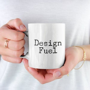 May include: White ceramic mug with a black inscription that reads "Design Fuel".