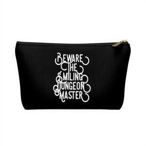 May include: Black canvas zippered pouch with white text that reads "Beware the Smiling Dungeon Master".