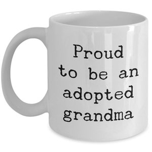 May include: White ceramic coffee mug with black text that reads "Proud to be an adopted grandma".