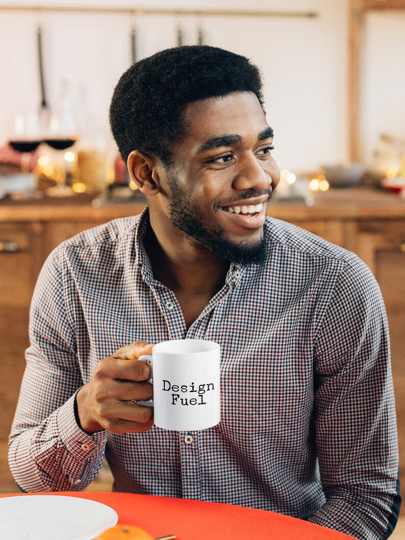 May include: A person holding a white ceramic mug with the text "Design Fuel" in black lettering.