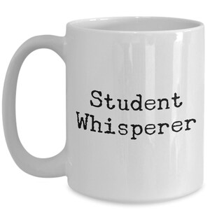 May include: White ceramic coffee mug with a black inscription that reads "Student Whisperer".