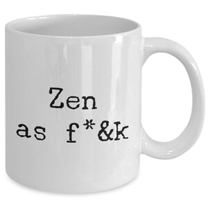 May include: White ceramic mug with a curved handle. The mug features the text "Zen as f*&k" in black, bold, sans-serif font. The mug is a standard size for coffee or tea.