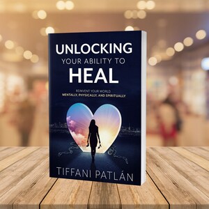 Könnte beinhalten: Ein Buchcover mit dunkelblauem Hintergrund und dem Titel "Unlocking Your Ability to Heal". Der Untertitel lautet "Reinvent Your World Mentally, Physically, and Spiritually". Das Cover zeigt eine Silhouette einer Frau, die durch eine herzförmige Tür geht, mit einer Stadt im Hintergrund.