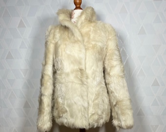 May include: A white faux fur jacket with a collar and long sleeves. The jacket is displayed on a wooden mannequin.