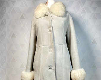 May include: A white sheepskin coat with a large white fur collar and cuffs. The coat has a button closure and a long, fitted silhouette.