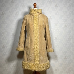 May include: A long, tan suede coat with a faux fur collar and trim. The coat has a zipper closure and is lined with a soft, white fabric.