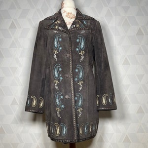 May include: A brown suede jacket with a paisley pattern embroidered on the front and sleeves. The jacket has a collar and a button closure.