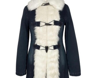Può includere: Un cappotto in denim blu scuro con colletto e pannello frontale in ecopelliccia bianca. Il cappotto presenta chiusure con fibbia nere ed è esposto su un manichino di legno. Un elegante capo di abbigliamento.
