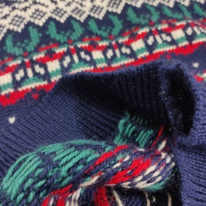 Puede incluir: Primer plano de un su&eacute;ter azul de punto con un patr&oacute;n geom&eacute;trico blanco, rojo y verde. El su&eacute;ter est&aacute; doblado por la mitad, mostrando el interior de la tela.