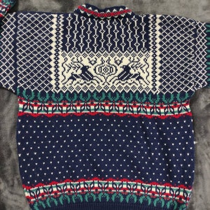 Puede incluir: Un su&eacute;ter de punto azul con un dise&ntilde;o estampado en blanco, rojo y verde. El su&eacute;ter presenta un dise&ntilde;o escandinavo tradicional con renos y patrones geom&eacute;tricos.