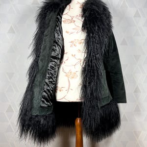 May include: A black suede coat with a long, fluffy black fur collar and trim. The coat is lined with a black satin fabric.