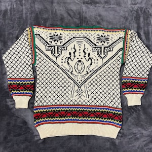 May include: A cream-coloured knitted sweater with a black and white geometric pattern. The sweater has a red, yellow, blue and green border around the neck and bottom.