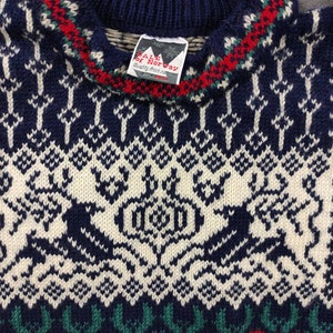 Puede incluir: Un su&eacute;ter de punto azul y blanco con un patr&oacute;n tradicional noruego. El su&eacute;ter tiene un ribete rojo, verde y blanco alrededor del cuello. La etiqueta en el su&eacute;ter dice "Dale of Norway, Quality from Norway".