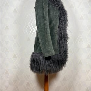 May include: A dark green suede coat with a black faux fur collar, trim, and lining. The coat is long and has a fitted silhouette.