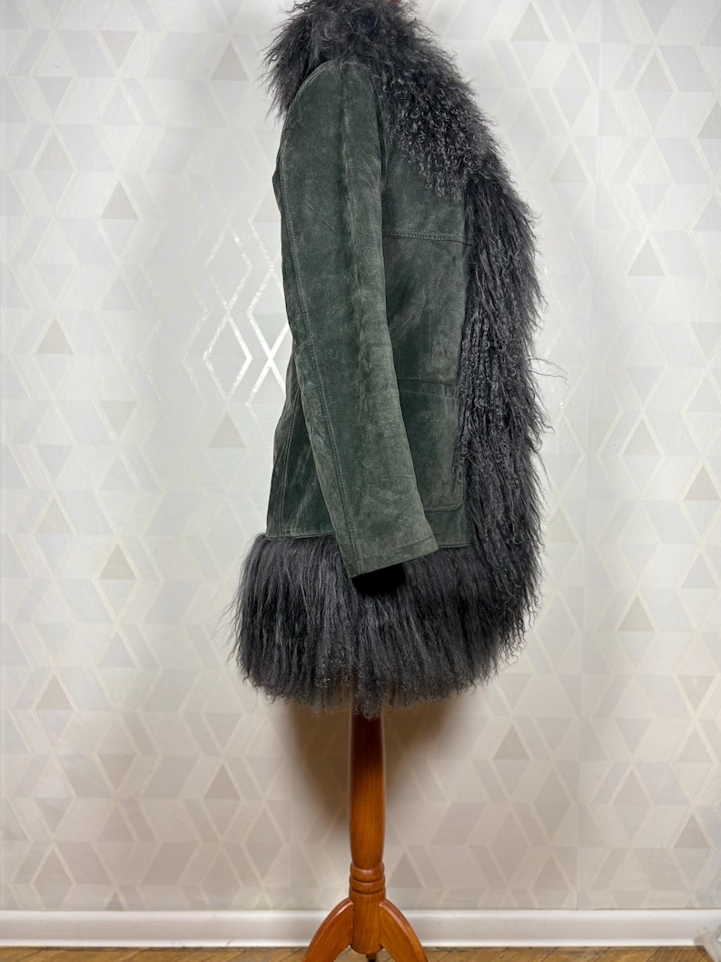 May include: A dark green suede coat with a black faux fur collar, trim, and lining. The coat is long and has a fitted silhouette.