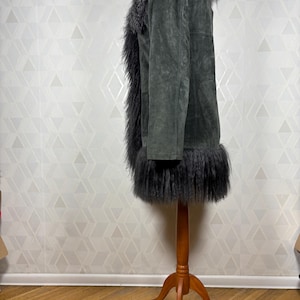 May include: A dark gray suede jacket with a long, fluffy black faux fur collar and trim. The jacket is on a wooden mannequin.