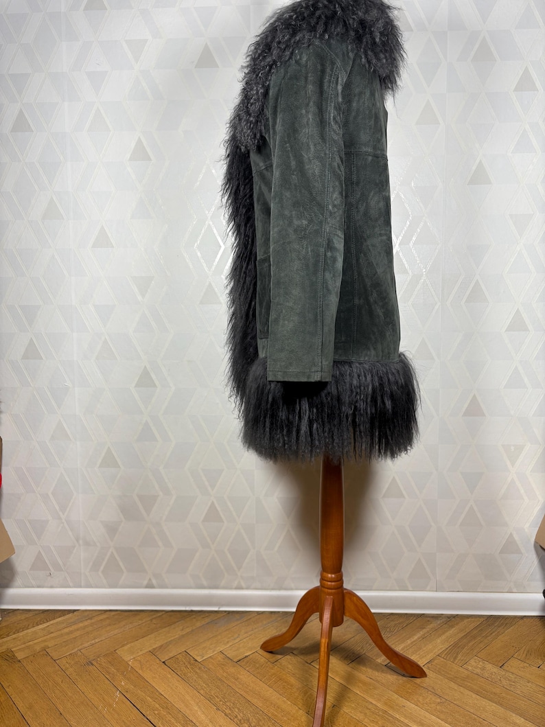 May include: A dark gray suede jacket with a long, fluffy black faux fur collar and trim. The jacket is on a wooden mannequin.