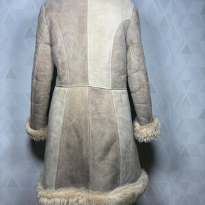 Puede incluir: Abrigo de ante beige con cuello, pu&ntilde;os y dobladillo de borrego color crema. El abrigo tiene un corte entallado con paneles verticales y mangas largas. Vista trasera del abrigo, ideal para el clima fr&iacute;o.