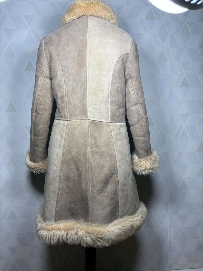 Puede incluir: Abrigo de ante beige con cuello, pu&ntilde;os y dobladillo de borrego color crema. El abrigo tiene un corte entallado con paneles verticales y mangas largas. Vista trasera del abrigo, ideal para el clima fr&iacute;o.