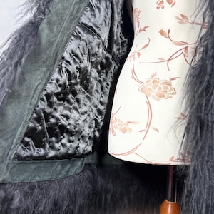 May include: A black faux fur jacket with a dark green suede lining. The jacket is open and the lining is visible. The jacket is on a white mannequin with a floral pattern.