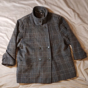 May include: A double-breasted, grey and brown tweed jacket with a high collar and two pockets.