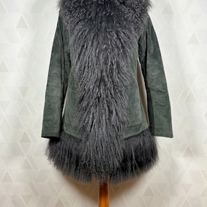 May include: A long, dark green suede coat with a large, fluffy gray fur collar and trim. The coat has a long, flowing silhouette and a relaxed fit.