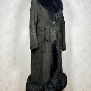 Puede incluir: Abrigo largo de ante verde oscuro con cuello, pu&ntilde;os y ribetes de piel negra. El abrigo tiene cintur&oacute;n en la cintura y cierres de botones. El abrigo vintage se exhibe en un maniqu&iacute;.