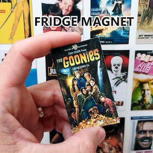 May include: A collection of fridge magnets featuring movie posters. The magnets include titles like "Kill Bill," "Dumb and Dumber," "Back to the Future," and "The Goonies." The text "FRIDGE MAGNET" is visible. The Goonies magnet is held in a hand.