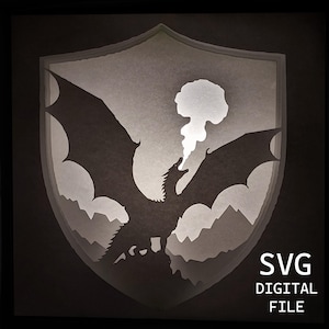 May include: A layered paper art piece featuring a dragon silhouette within a shield shape. The dragon is depicted with outstretched wings, mountains in the background, and a cloud of smoke. The text "SVG DIGITAL FILE" is visible.