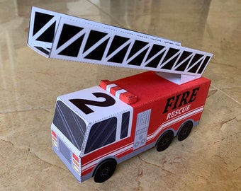 May include: A red and white paper fire truck model with a black ladder and the number 2 on the side. The truck says "FIRE RESCUE" on the side.