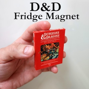 May include: A red D&D fridge magnet. The magnet features the text "D&D Fridge Magnet" at the top. The magnet is a miniature replica of a Dungeons & Dragons game box, with the words "DUNGEONS & DRAGONS" and "SET 1 BASIC RULES" visible.