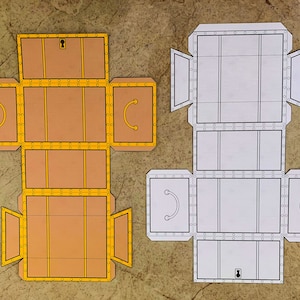 Puede incluir: Una plantilla imprimible para una caja de cart&oacute;n con una cerradura y un borde decorativo. La plantilla se muestra en dos versiones, una con fondo marr&oacute;n y otra con fondo blanco.