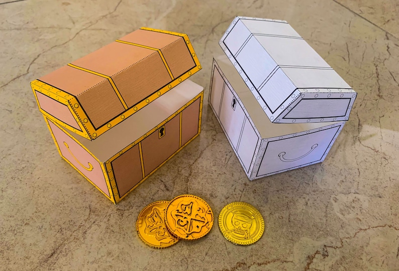 Puede incluir: Dos cofres del tesoro abiertos, uno marr&oacute;n y otro blanco, con monedas de oro sobre una superficie marr&oacute;n claro. Los cofres tienen un dise&ntilde;o decorativo con ribetes amarillos y detalles negros.