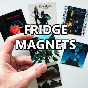 May include: A collection of fridge magnets featuring album art from various bands, including Black Sabbath, Fleetwood Mac, and Prince. The magnets are rectangular and colorful, with the words "FRIDGE MAGNETS" in large white letters.