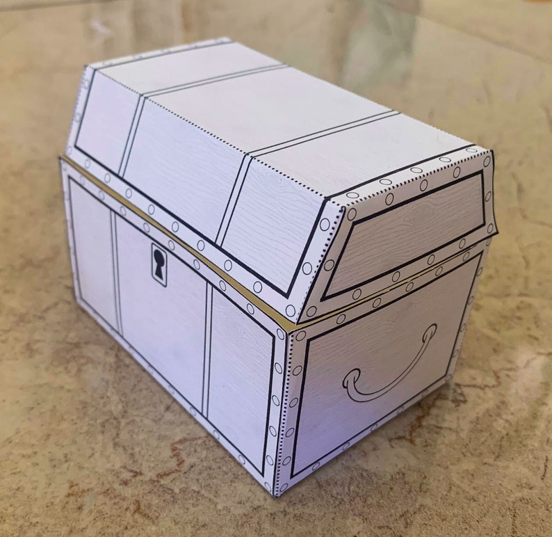 Puede incluir: Un cofre del tesoro de cart&oacute;n blanco con un borde dorado y una cerradura. El cofre est&aacute; cerrado y tiene una manija en el lateral.