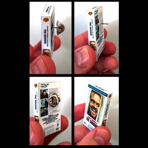 May include: A miniature VHS tape replica of the movie "The Shining" by Stanley Kubrick. The tape is blue and white with a picture of Jack Nicholson on the front. The tape is attached to a pin.