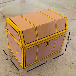 Puede incluir: Un cofre del tesoro de cart&oacute;n con un dise&ntilde;o marr&oacute;n y amarillo. El cofre mide 2,5 pulgadas de ancho, 3,5 pulgadas de largo y 2 pulgadas de alto.