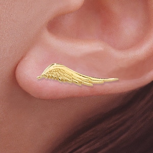 May include: Gold ear cuff with a wing design. The ear cuff is worn on the upper part of the ear. The text "The Ear Pin. for pierced & non-pierced ears" is visible at the top of the image.