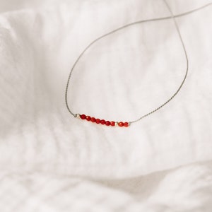 Puede incluir: Un collar delicado con una sola fila de pequeñas cuentas rojas en un cordón gris fino.