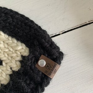May include: Black and white knitted hat with a brown leather tag that says "The Unraveled Sheep".